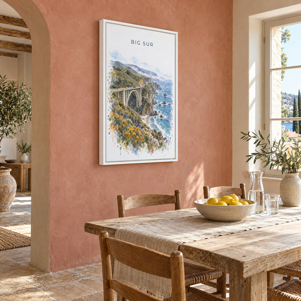 Big Sur watercolor print as a white floater canvas on a terracotta wall above a rustic dining table