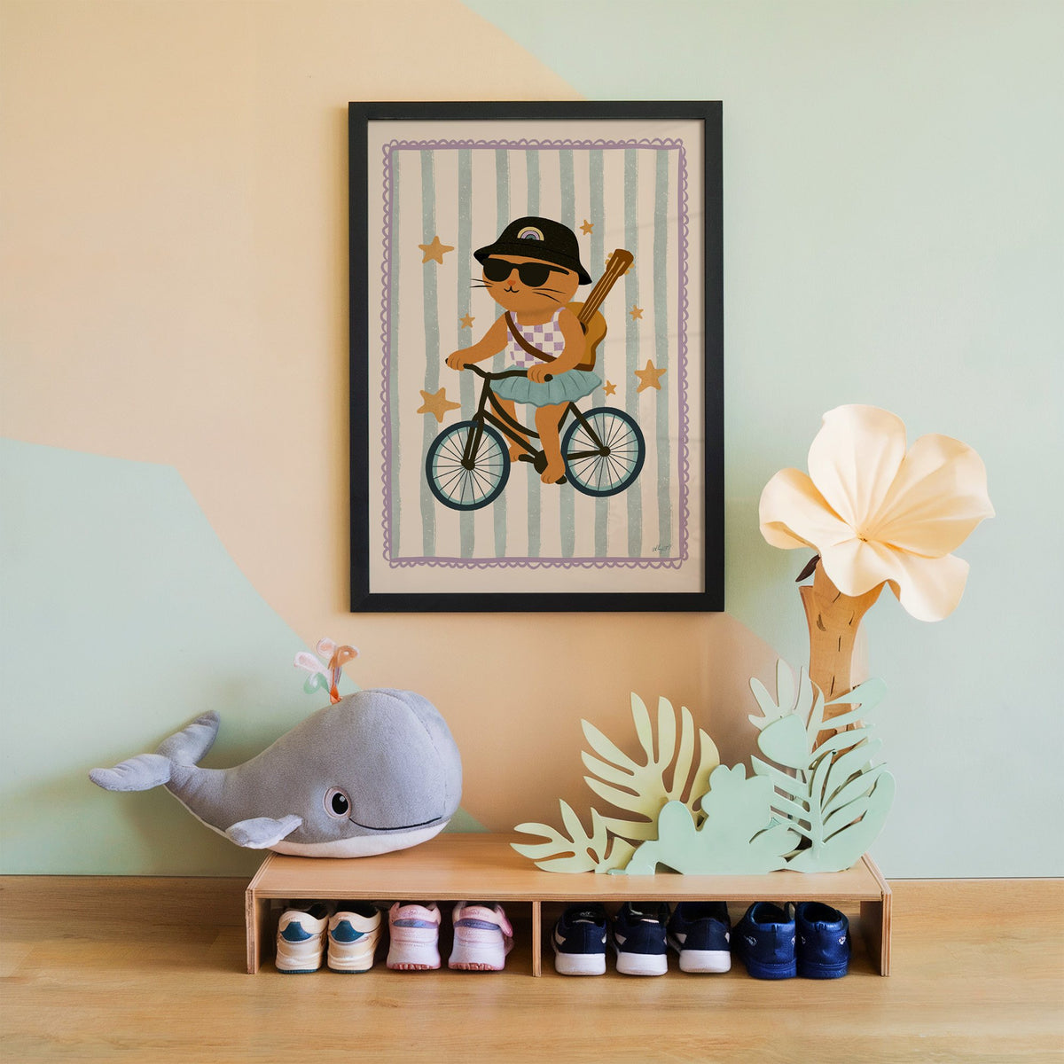 Orange cat on bicycle with ukulele nursery print in a black frame on a mint and peach wall above a whale plush