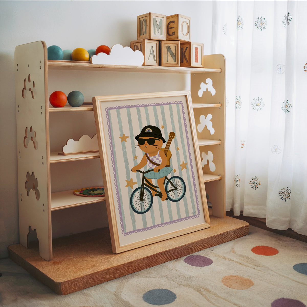 Orange cat on bicycle with ukulele nursery print in an oak frame leaning on a toy shelf with wooden letter blocks