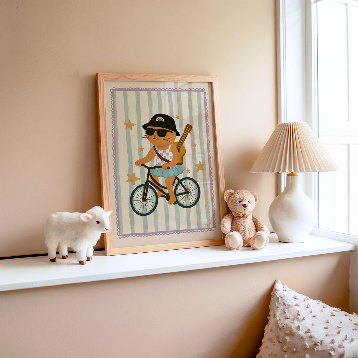 Orange cat on bicycle with ukulele nursery print in an oak frame on a window ledge with a toy lamb and teddy