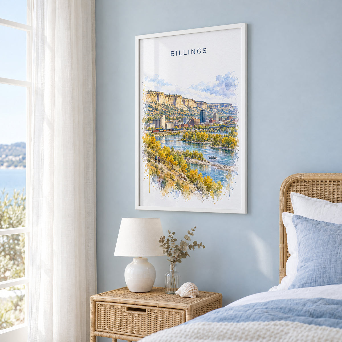 Billings watercolor print in a white frame on a pale blue wall beside a rattan bed in a coastal bedroom