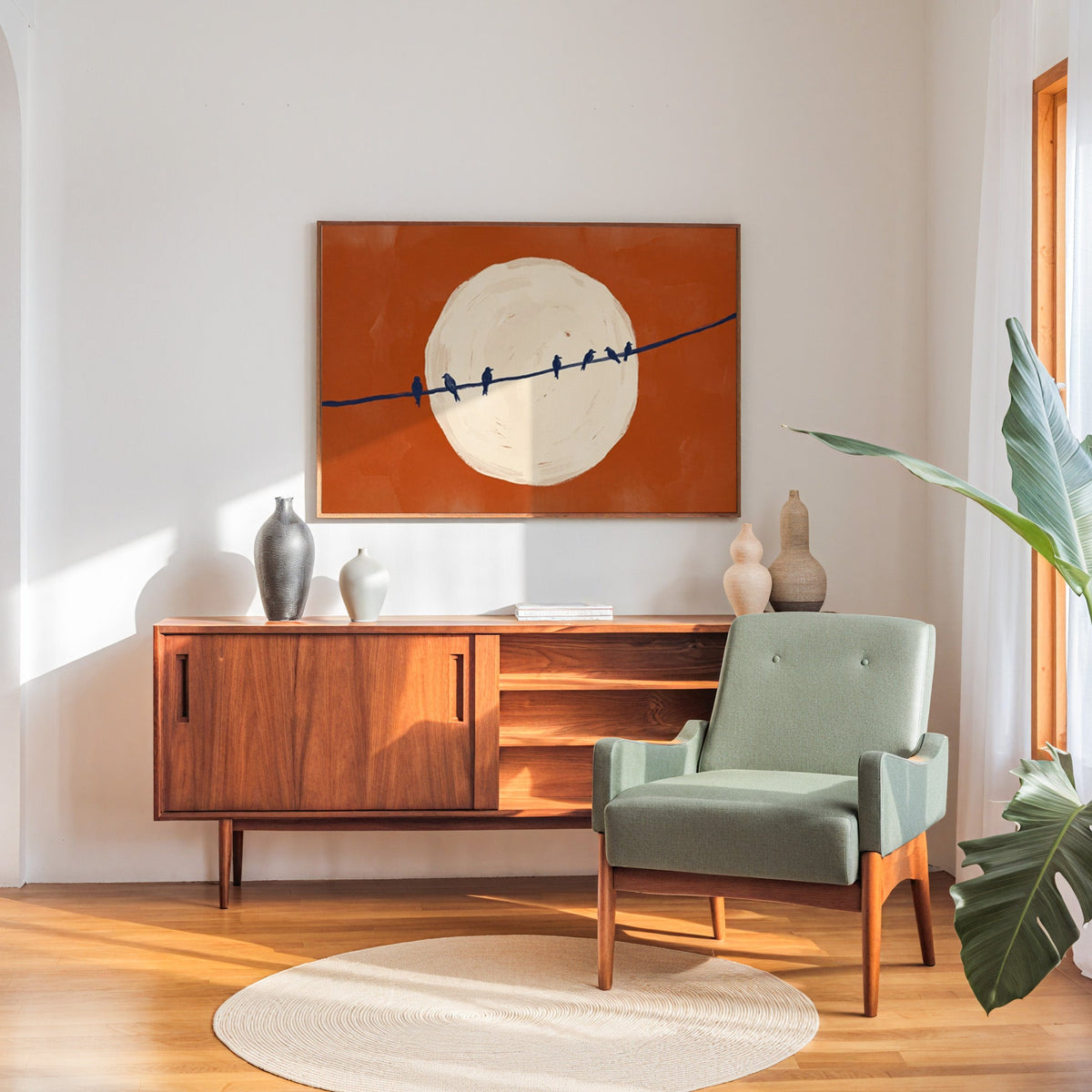 Minimalist bird print in a walnut frame above a sideboard beside a sage armchair
