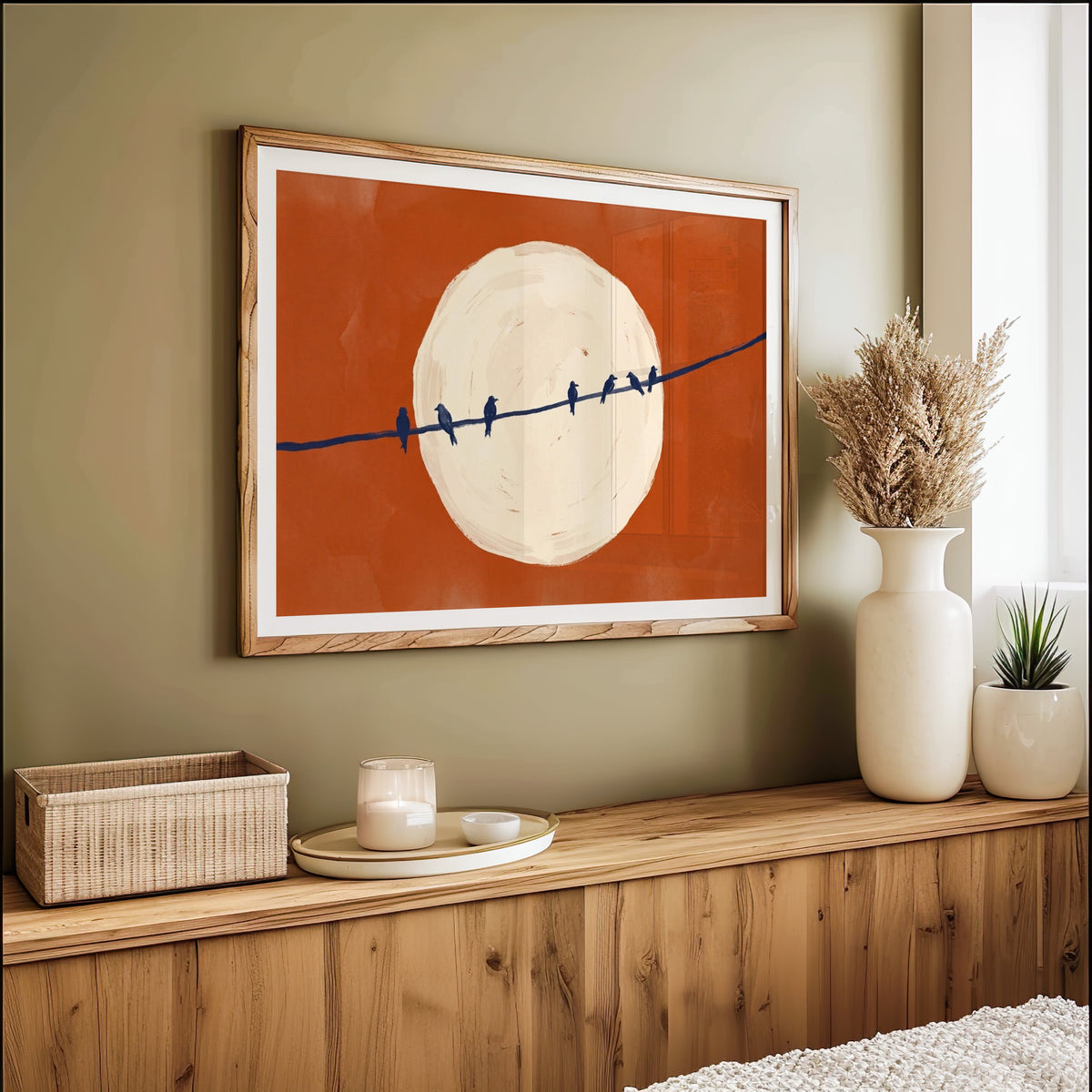 Birds on a wire moon print in an oak frame on an olive green wall above pampas grass