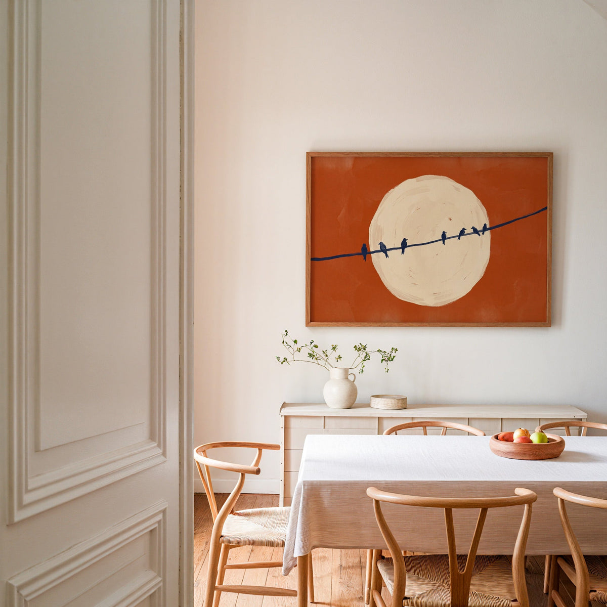 Birds on wire silhouette print in an oak frame in a dining room with wishbone chairs