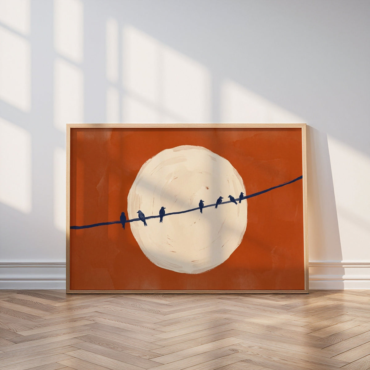Minimalist bird print in an oak frame leaning on a parquet floor in window light
