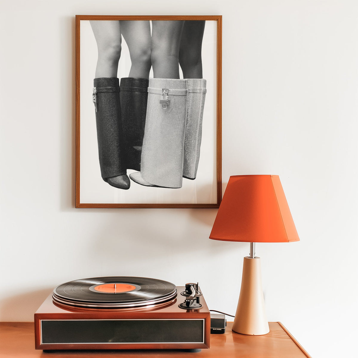 Black and silver crystal knee-high boots print in a walnut frame above a record player and orange lamp