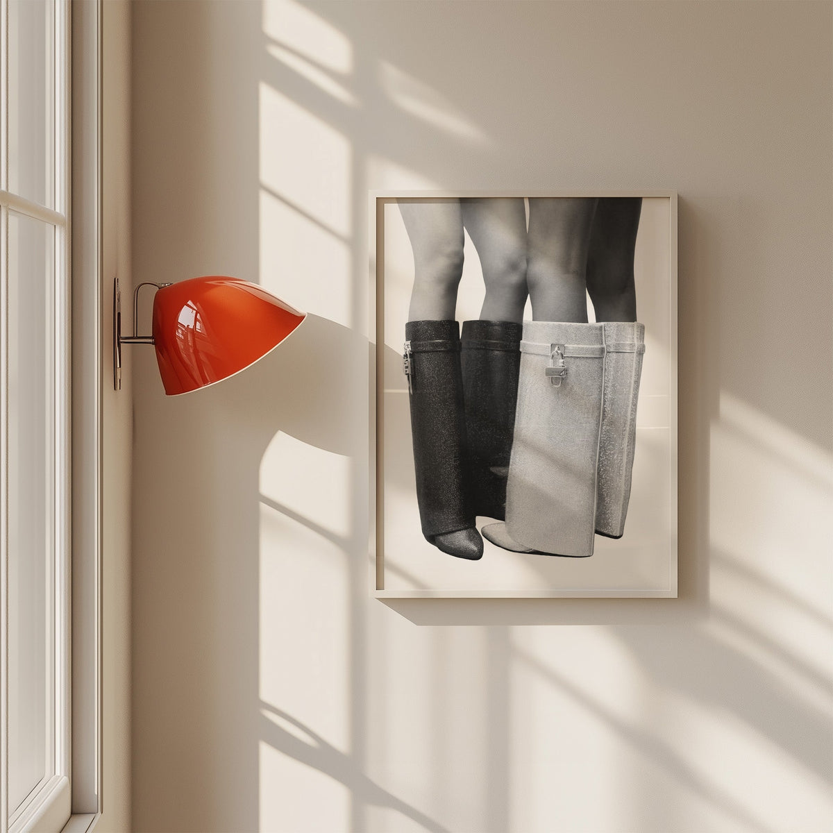 Black and silver crystal knee-high boots print in a white frame on a sunlit wall beside a red sconce