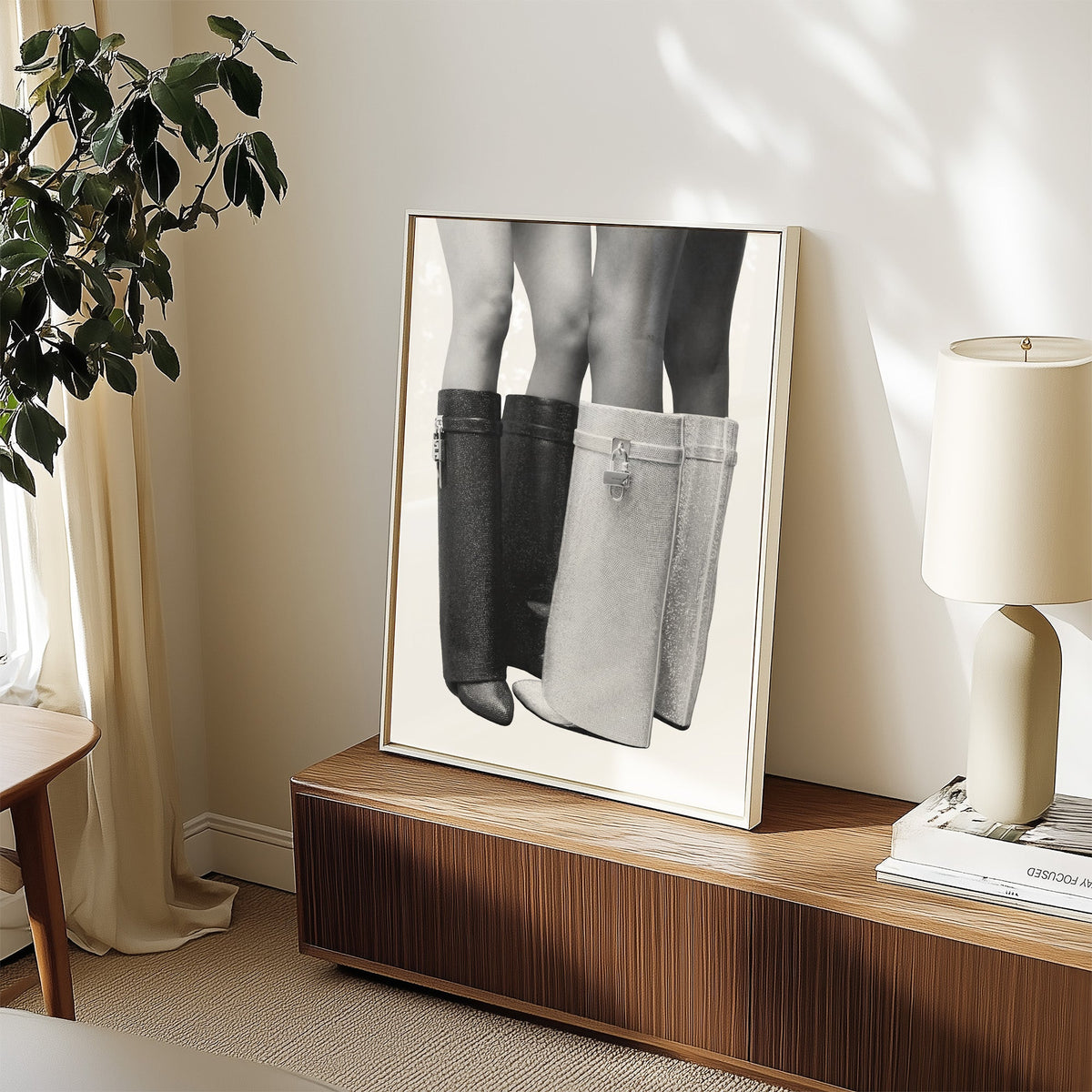 Black and silver crystal knee-high boots print in a white frame on a walnut sideboard beside a ceramic lamp