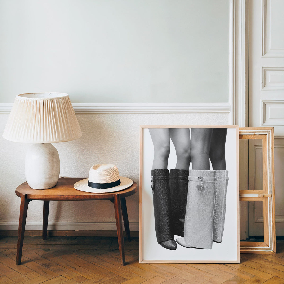 Black and silver crystal knee-high boots print in a pine frame on a wood floor beside a lamp and straw hat
