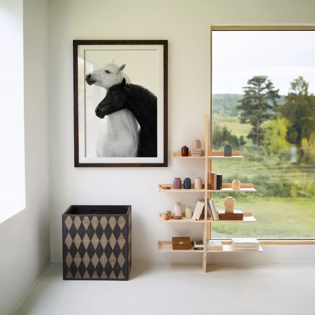 White horse and black horse necks crossed print in a walnut frame with a white mat beside wooden shelves and a garden window