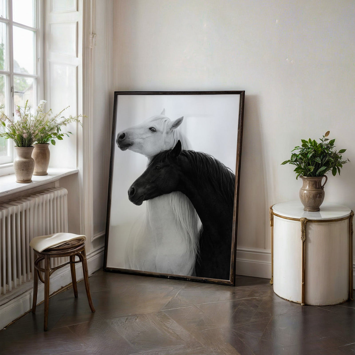 White horse and black horse necks crossed print in a black frame on a dark stone floor beside a white side table