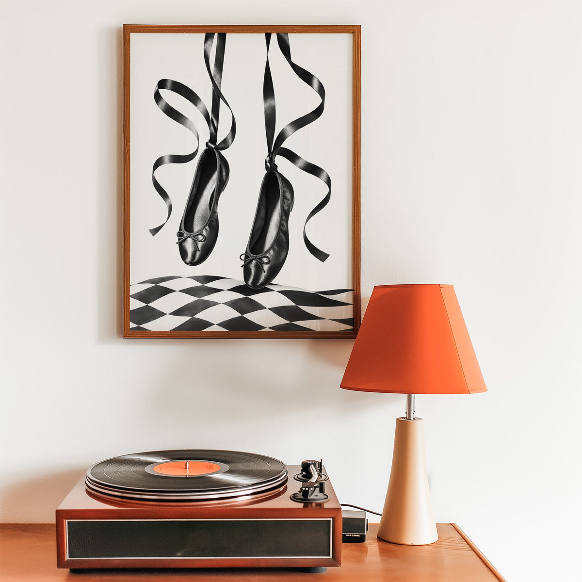 Black ballet flats on ribbons over checkerboard print in a walnut frame above a record player and orange lamp