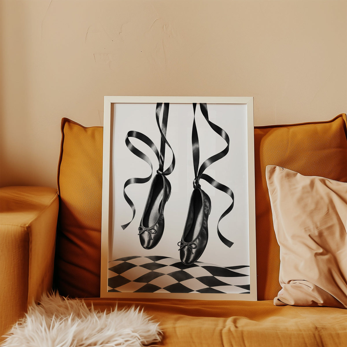 Black ballet flats on ribbons over checkerboard print in a white frame leaning on a mustard velvet sofa