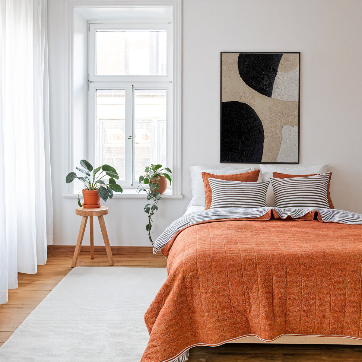 Black and beige textured shapes abstract print in a thin black frame above a bed with a rust orange quilt