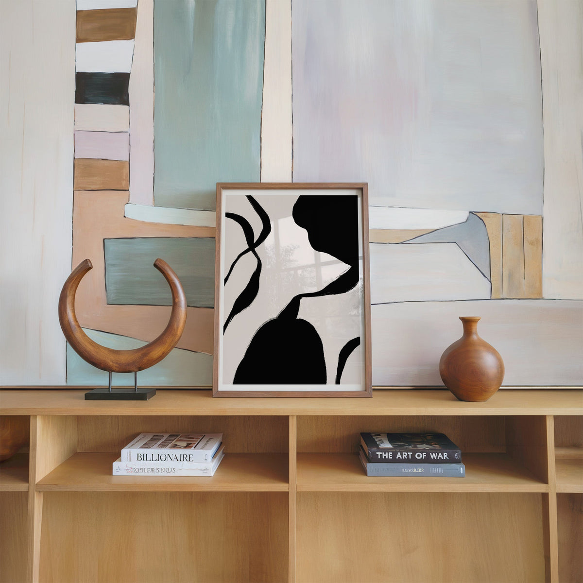 Black blob and hourglass lines on blush print in a walnut frame on an oak shelf beside a wooden crescent sculpture