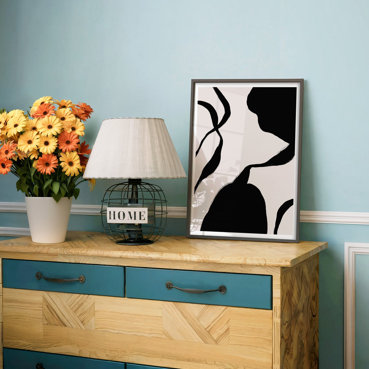 Black blob and hourglass lines on blush print in a charcoal frame on a teal dresser beside orange and yellow daisies
