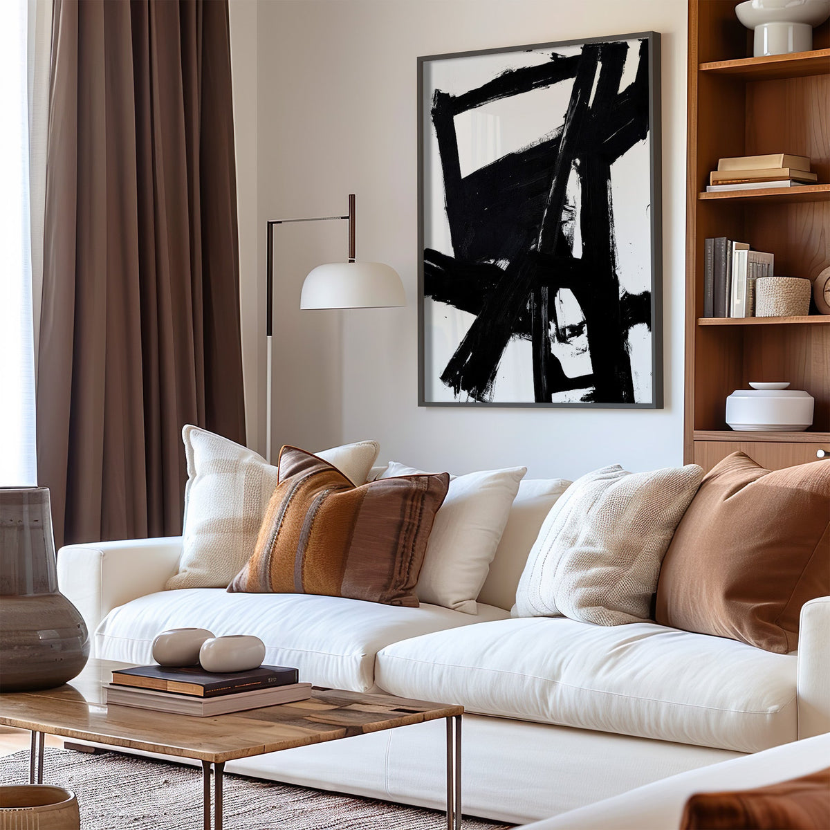 Black bold crossbeam brushstrokes on white print in a black frame above a cream sofa with brown striped pillows