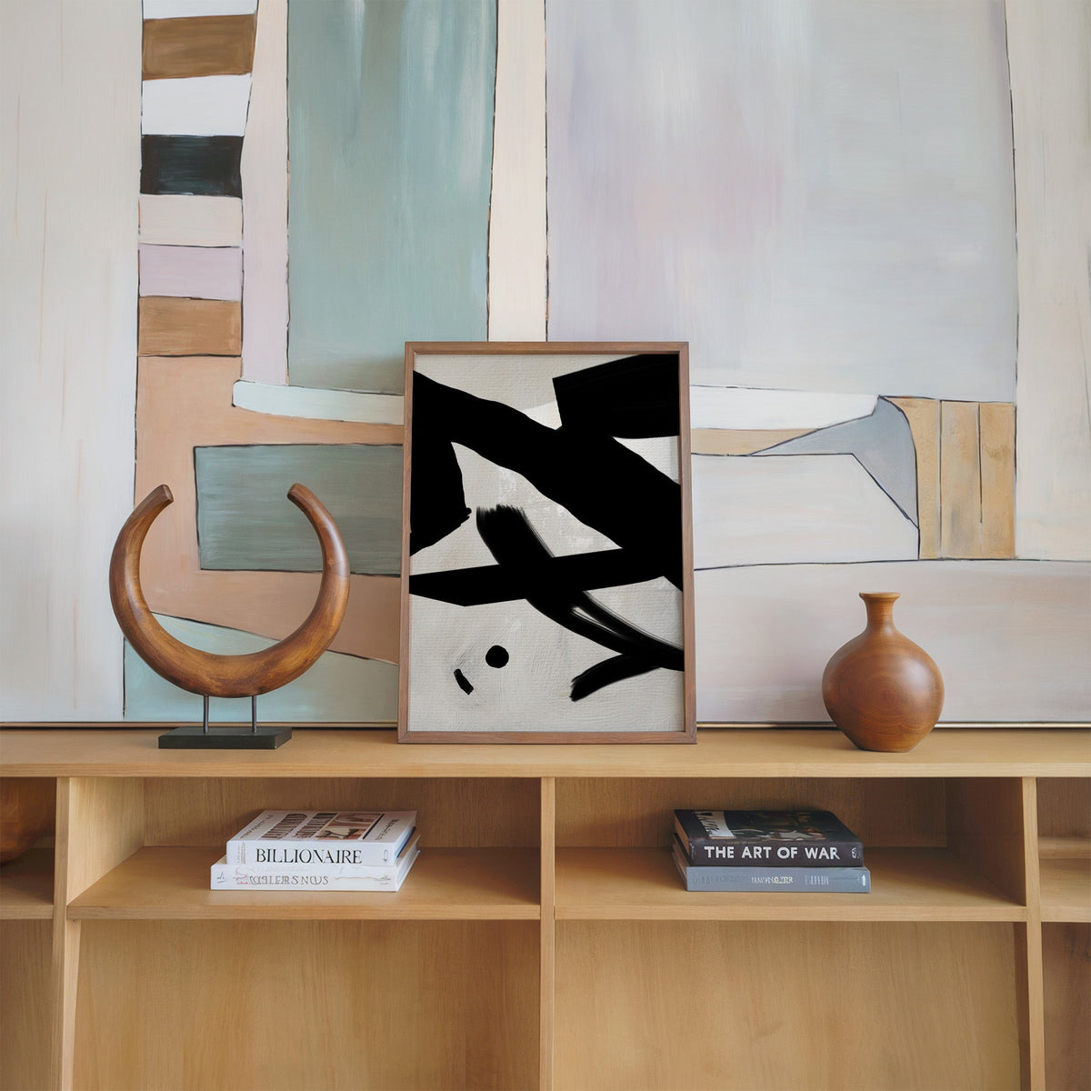 Black bold strokes and dot on cream linen print in a walnut frame on an oak shelf beside a wooden crescent sculpture