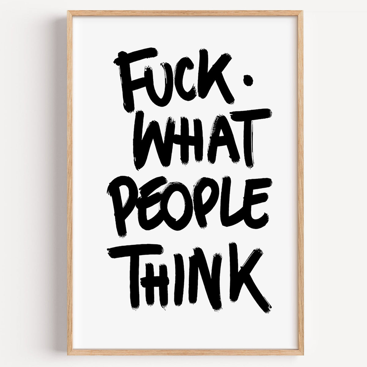Black brush lettering attitude quote print in a light oak frame on a plain white wall