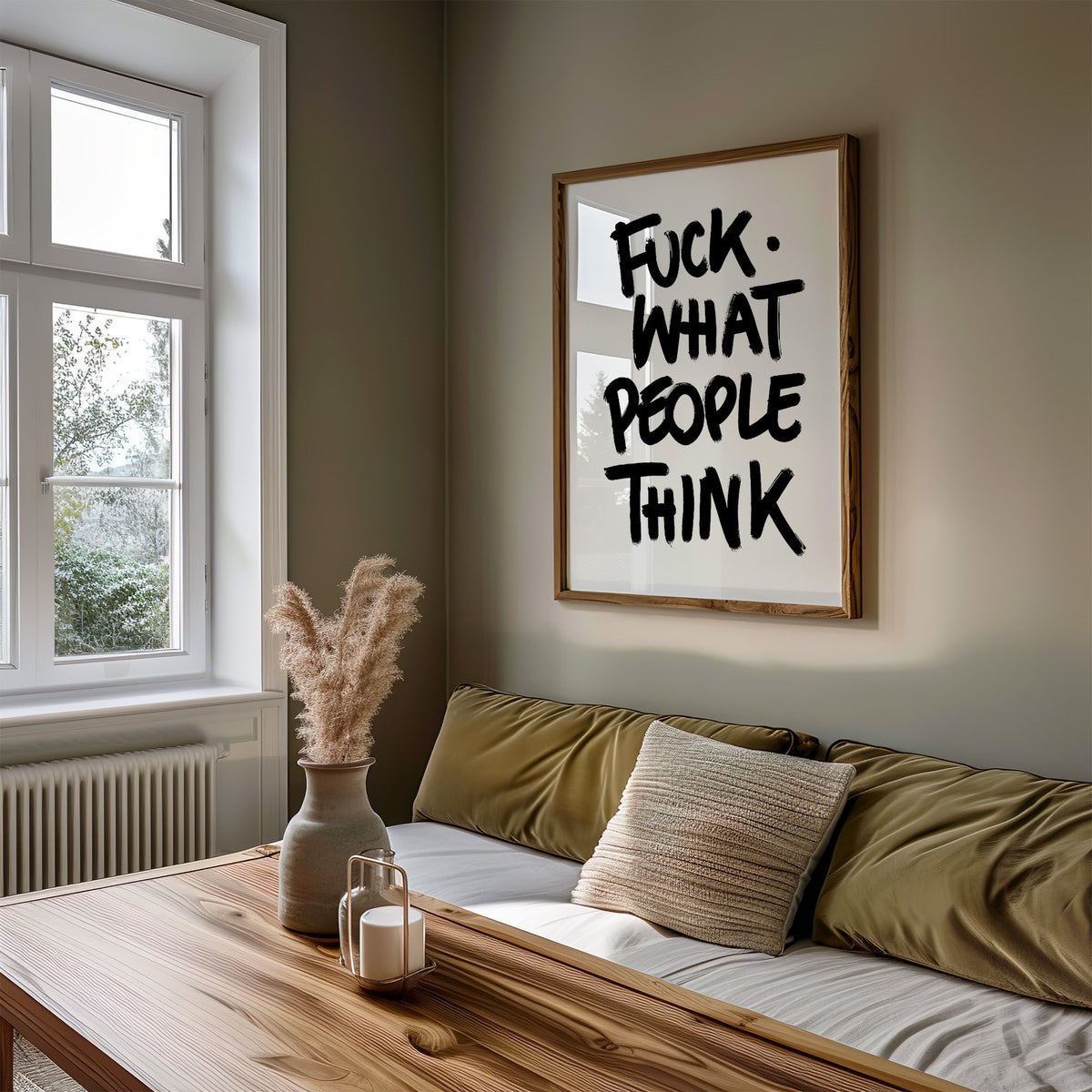 Black brush lettering attitude quote print in a walnut frame above an olive daybed by a window