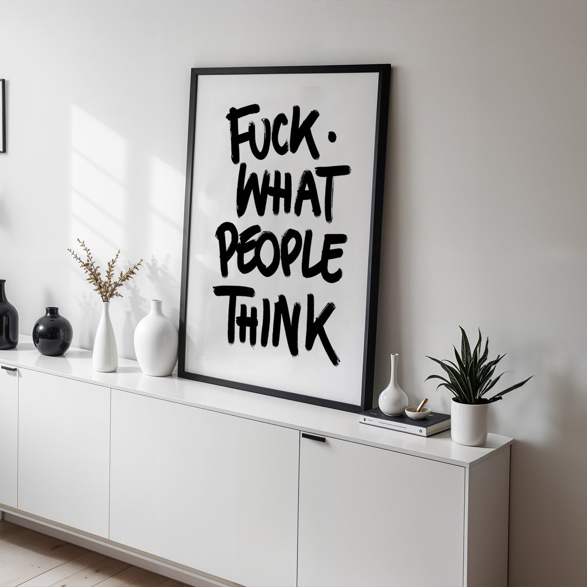 Black brush lettering attitude quote print in a black frame on a white sideboard with black and white vases