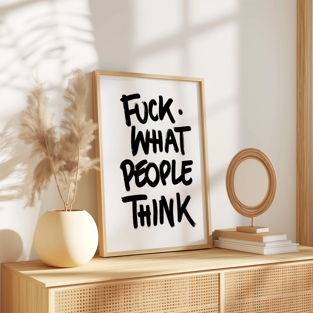 Black brush lettering attitude quote print in an oak frame on a rattan sideboard beside pampas grass