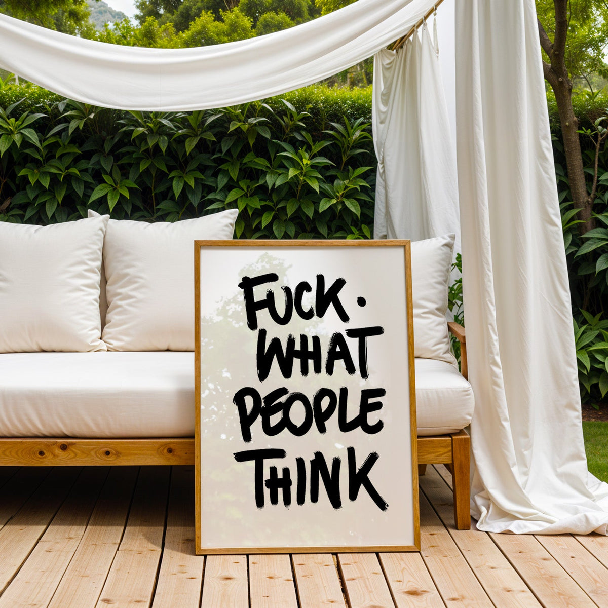 Black brush lettering attitude quote print in an oak frame on an outdoor daybed under white drapes