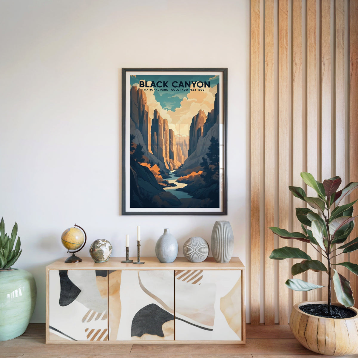 Black Canyon of the Gunnison print in a black frame above a light wood sideboard with a globe