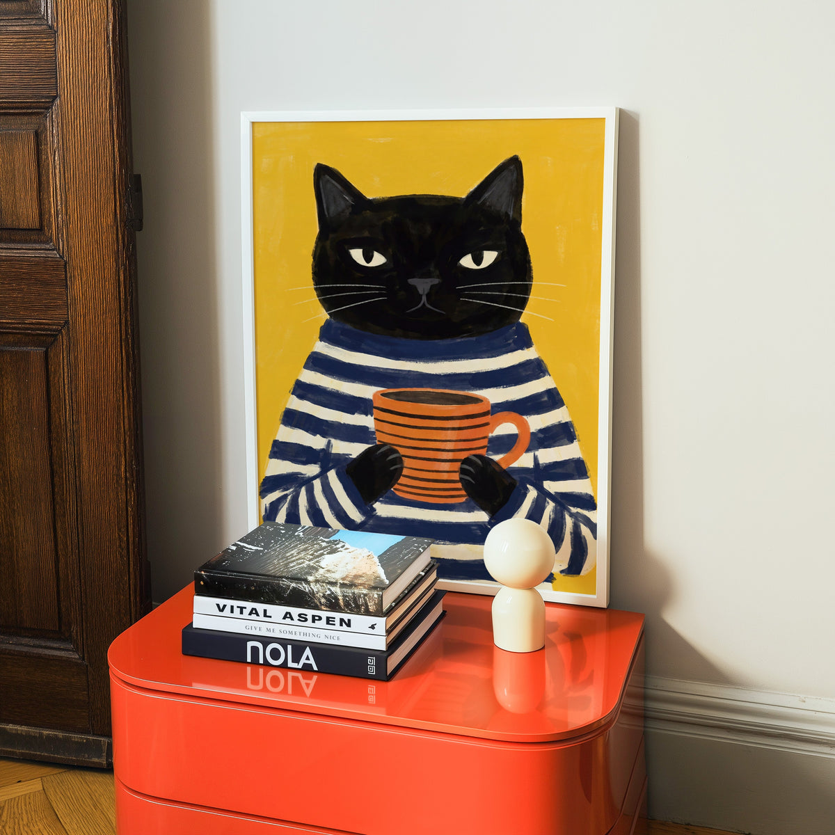 Cat in striped shirt print in a white frame on a glossy orange cabinet with books