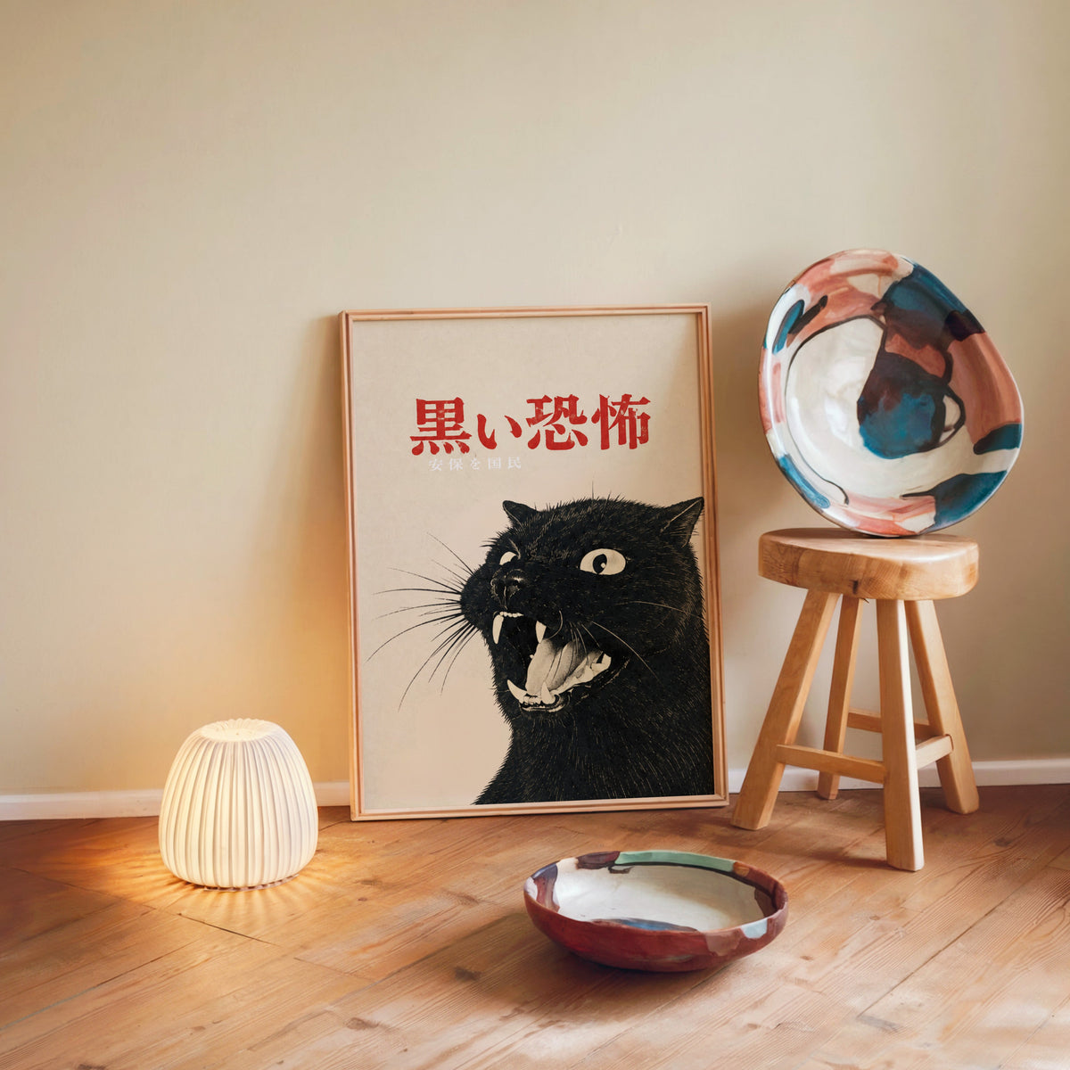 Hissing black cat kanji poster in a light wood frame leaning on a wooden floor by a glowing lamp and stool