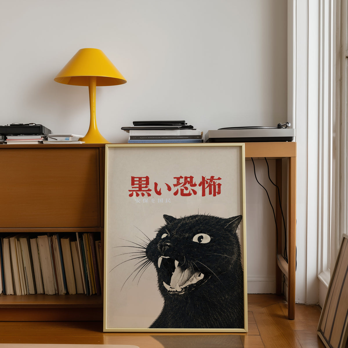 Hissing black cat kanji poster shown in a gold frame leaning under a teak desk with a yellow lamp