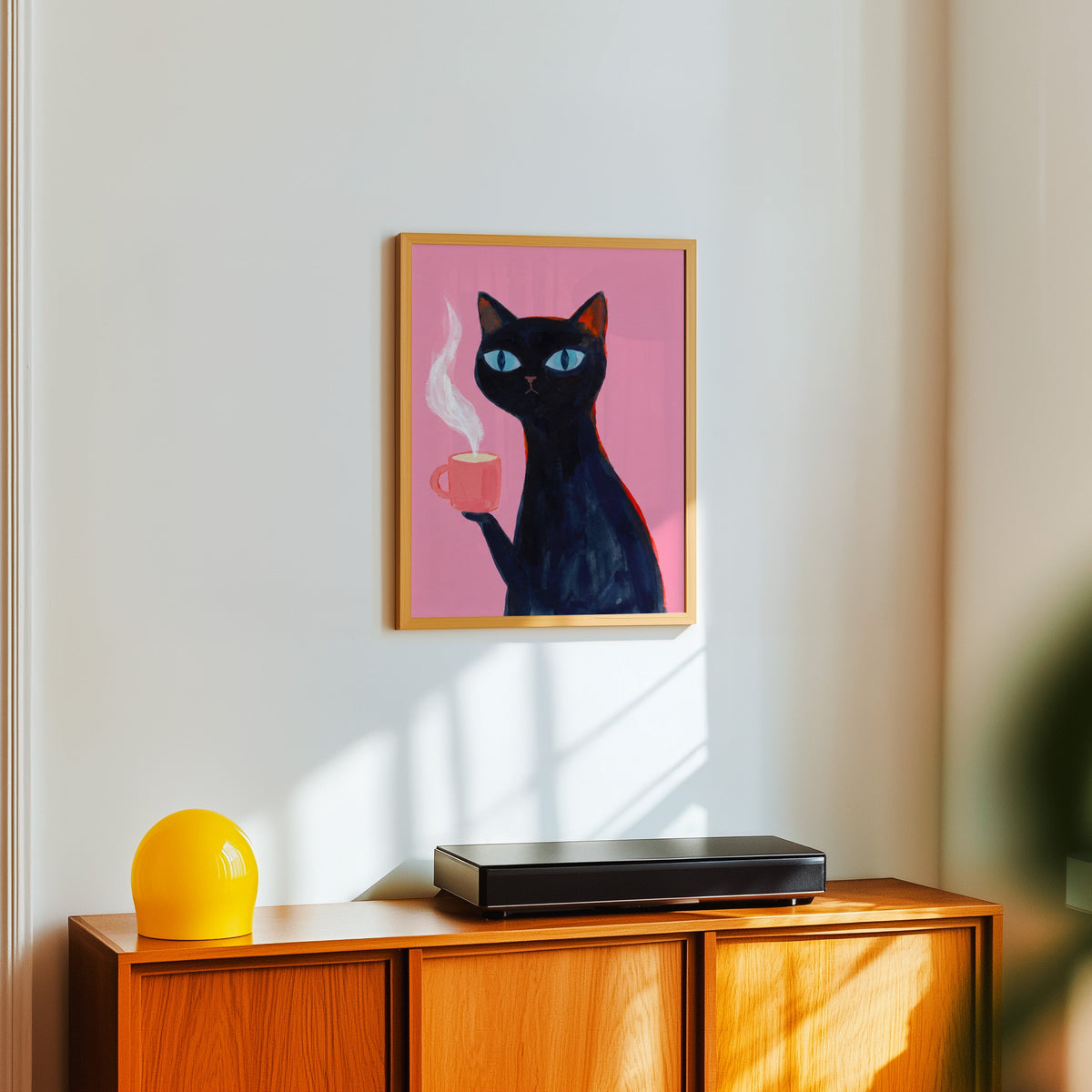 Blue-eyed black cat print in a light oak frame above a teak sideboard with a yellow lamp