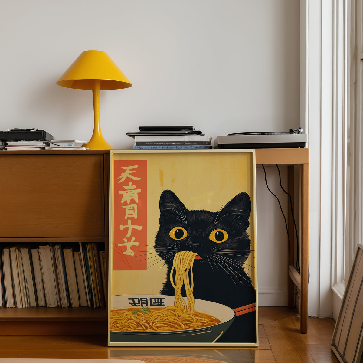 Black cat slurping ramen print shown in a gold frame below a teak desk with a yellow lamp