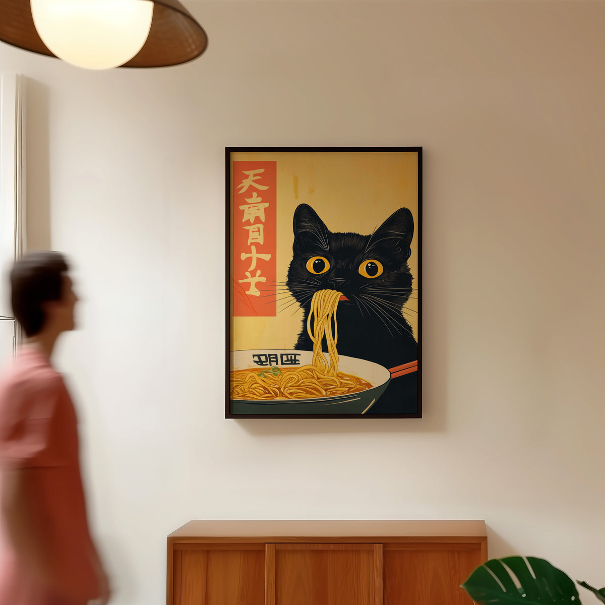 Black cat slurping ramen print in a black frame in a hallway under a rattan pendant