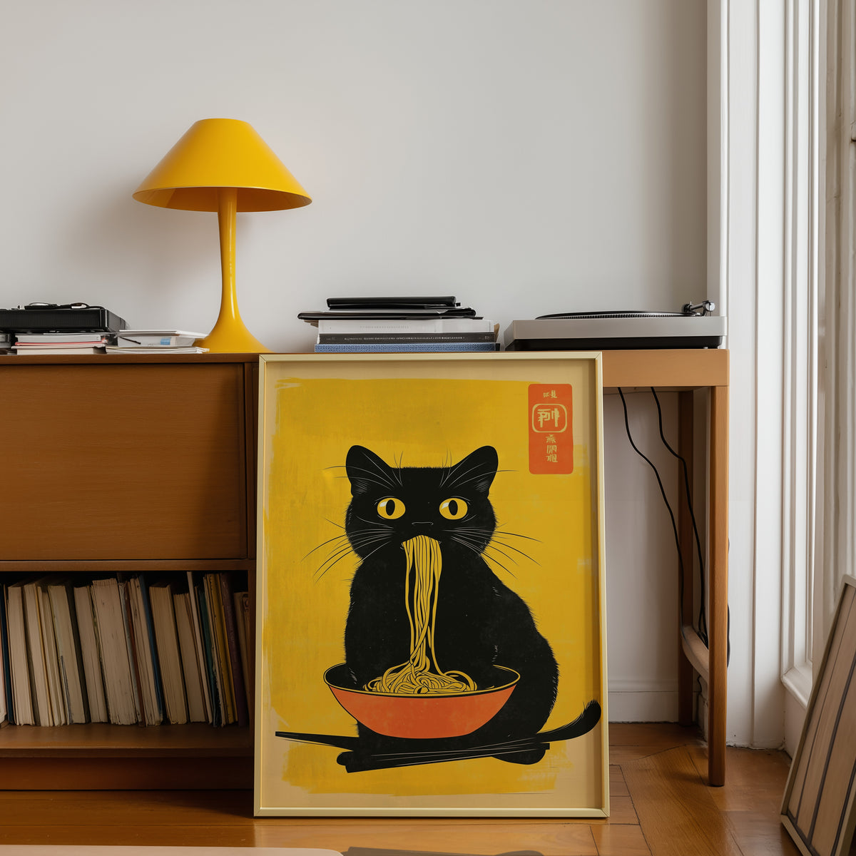 Black cat noodles orange bowl print shown in a gold frame below a teak desk with a yellow lamp