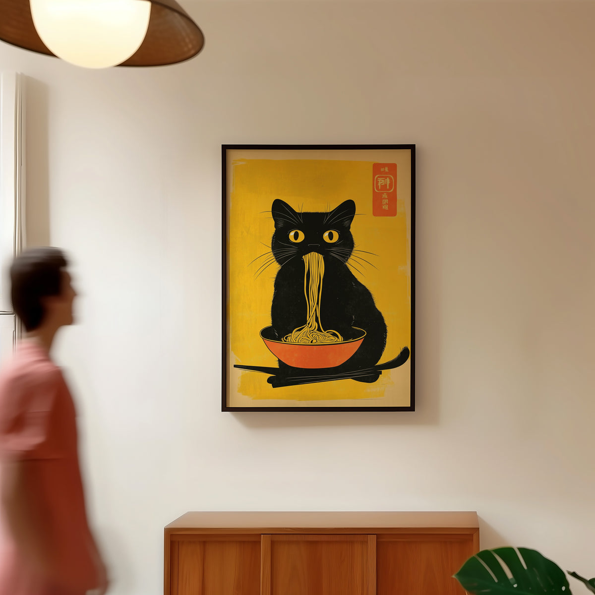 Black cat noodles orange bowl print in a black frame in a hallway under a rattan pendant