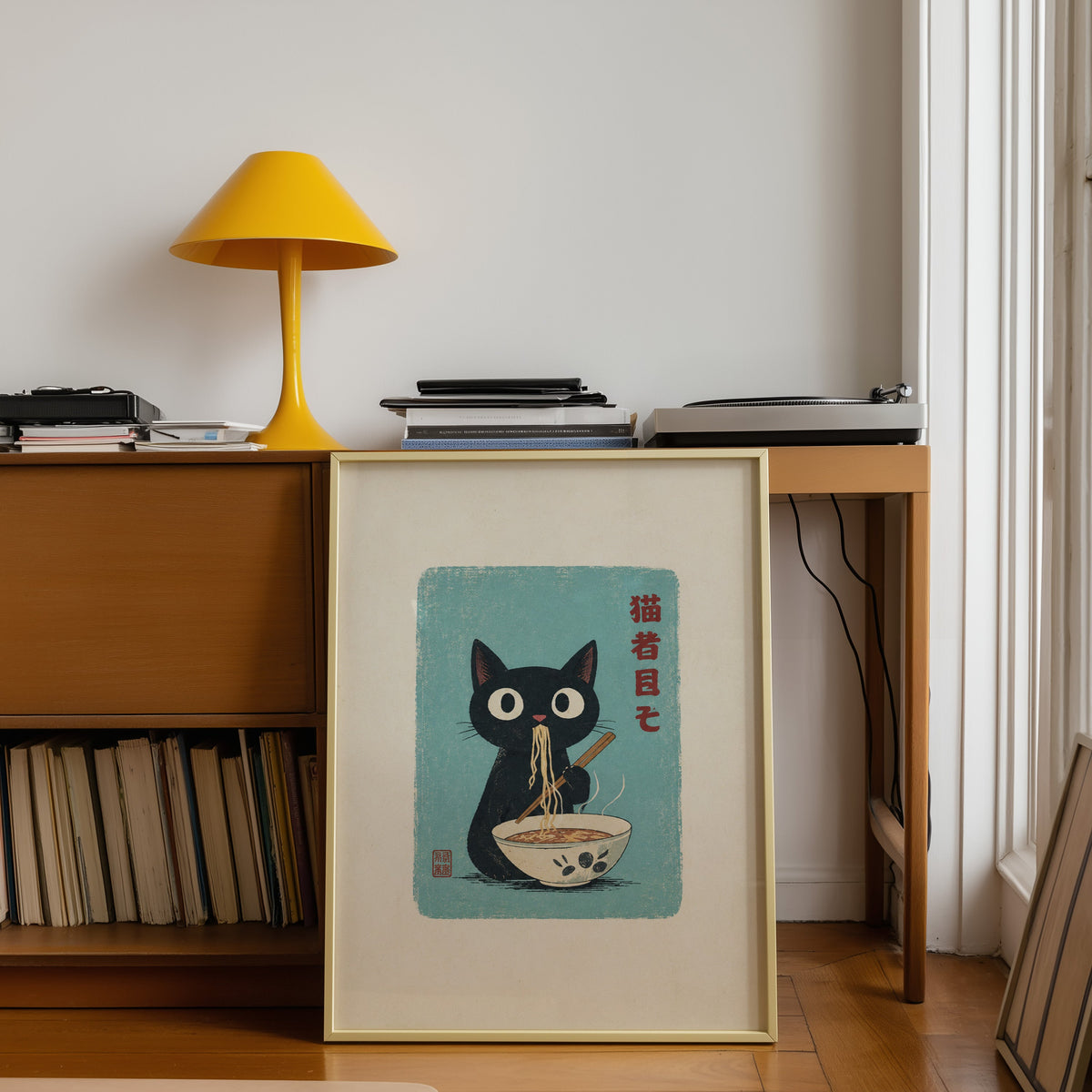 Black cat ramen teal poster shown in a gold frame leaning under a teak desk with a yellow lamp