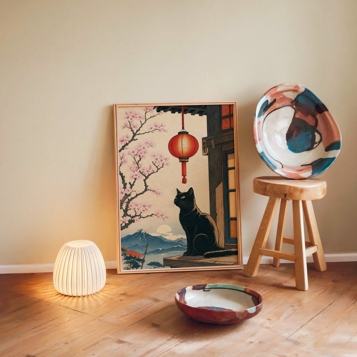 Black cat and red lantern poster in a light wood frame leaning on a wooden floor by a glowing lamp and stool