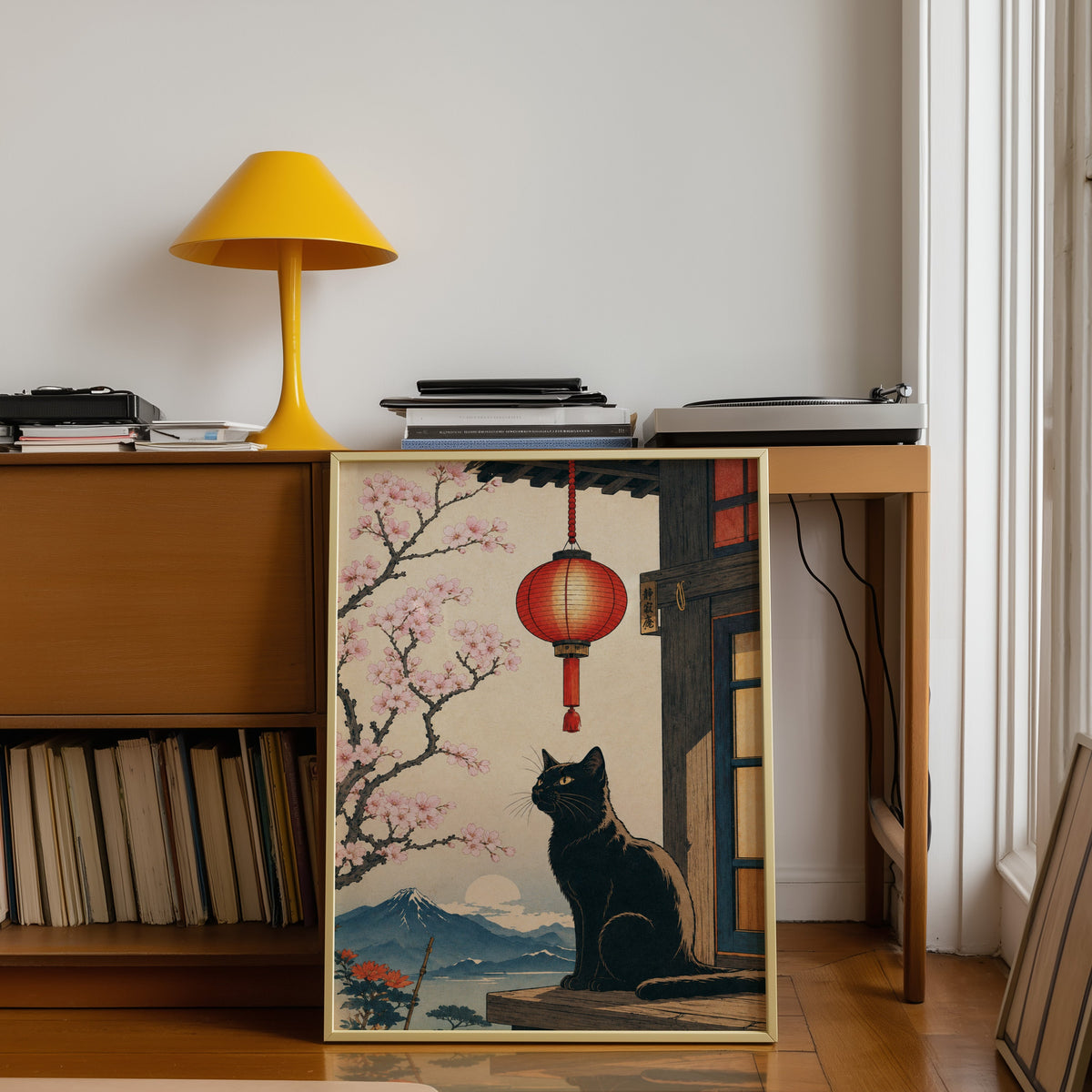 Black cat and red lantern poster shown in a gold frame leaning under a teak desk with a yellow lamp