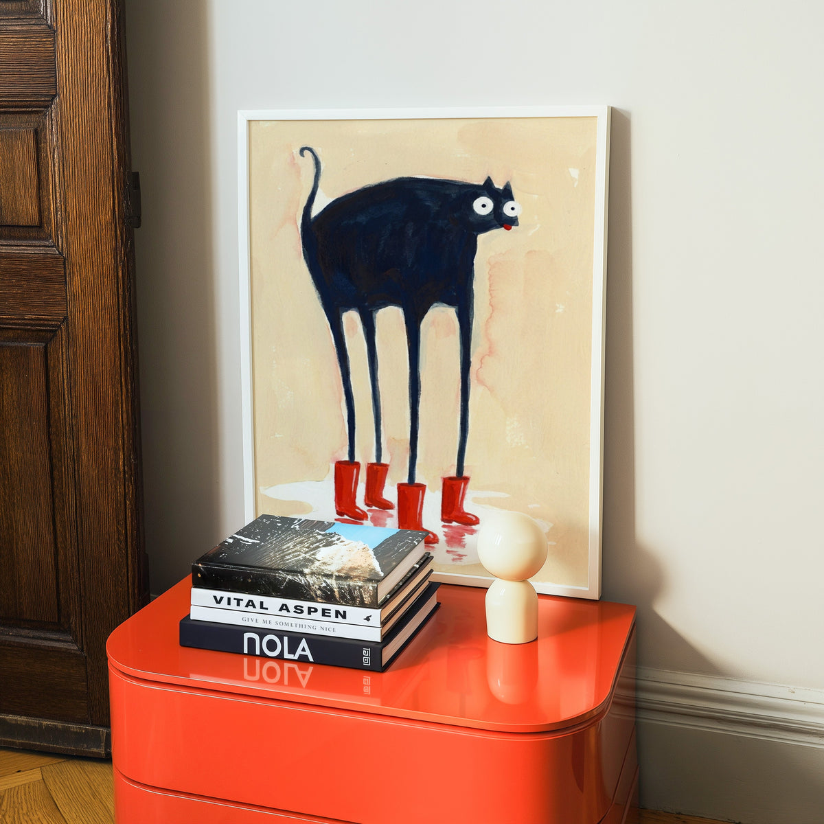 Funny cat in boots print in a white frame on a glossy orange cabinet with books