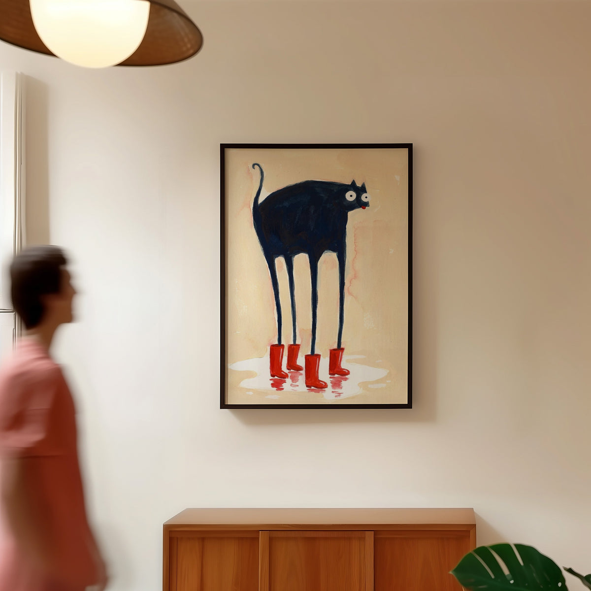 Red boots cat print in a black frame in a hallway under a rattan pendant