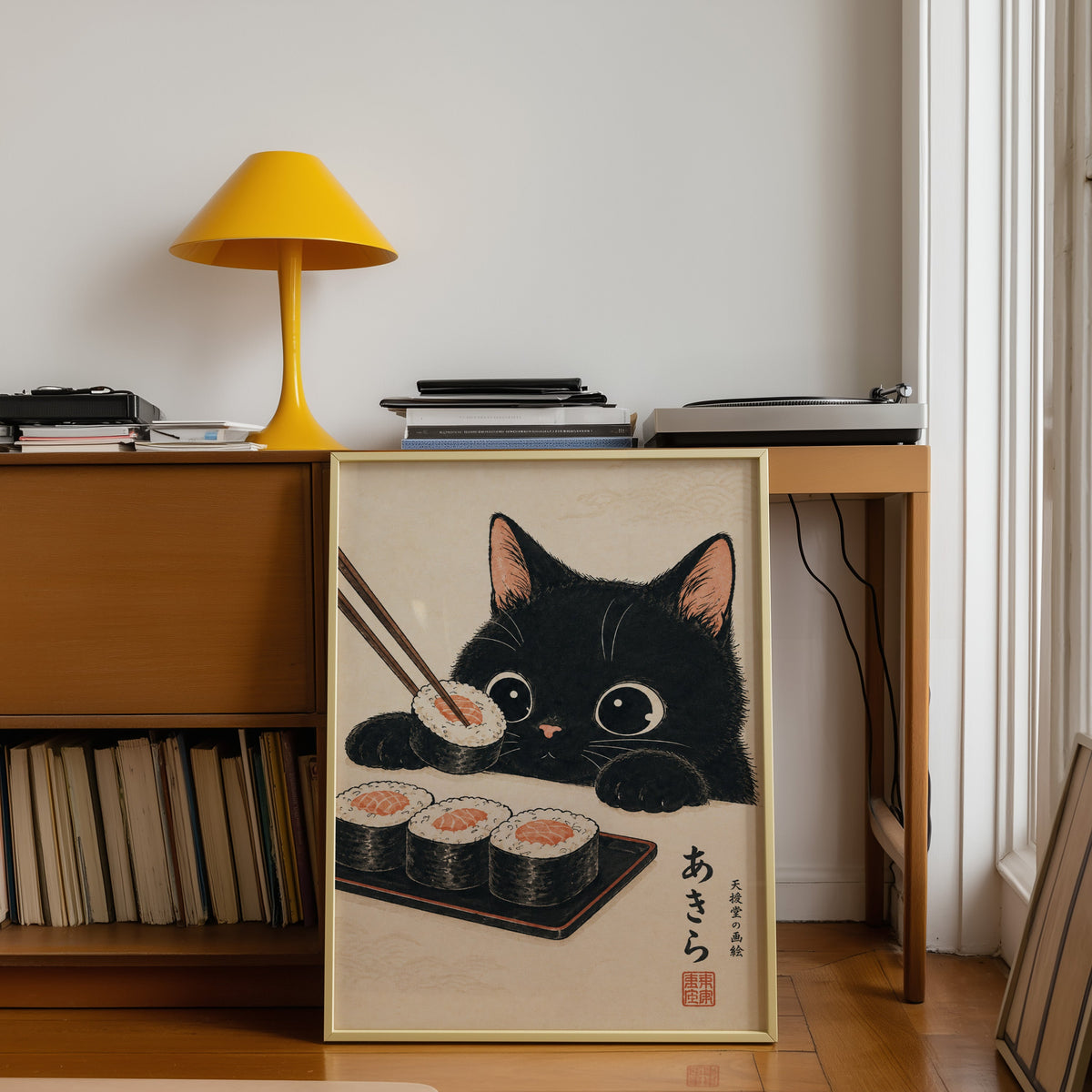 Black cat salmon sushi poster shown in a gold frame leaning under a teak desk with a yellow lamp
