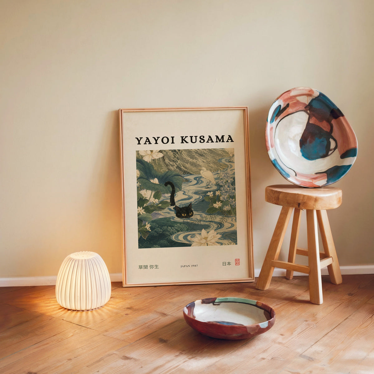 Black cat swimming lotus river poster in a light wood frame leaning on a wooden floor by a glowing lamp and stool