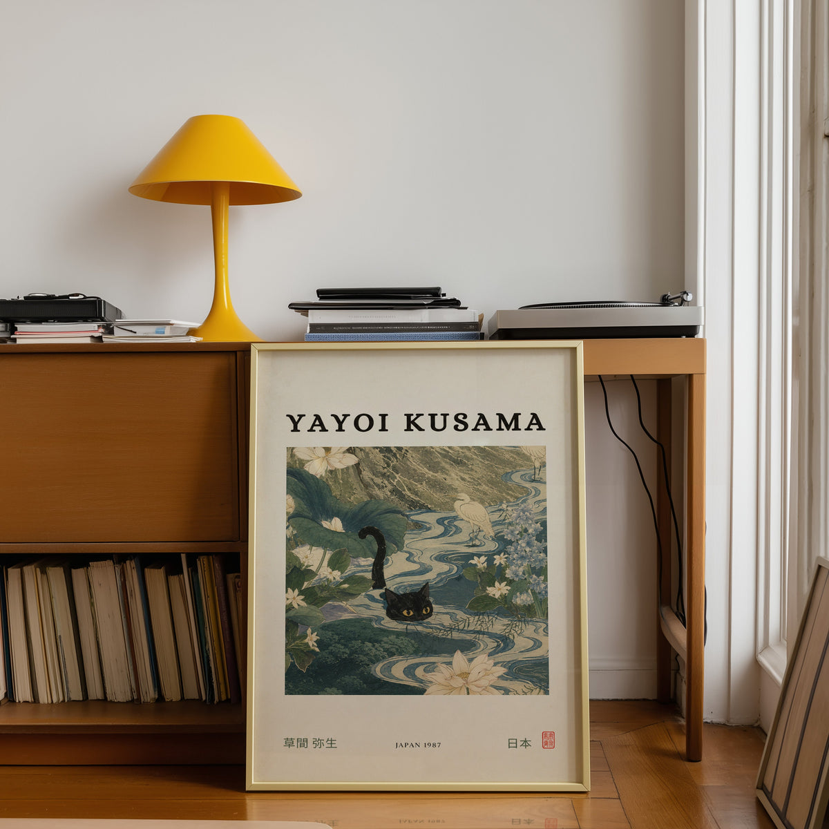 Black cat swimming lotus river poster shown in a gold frame leaning under a teak desk with a yellow lamp