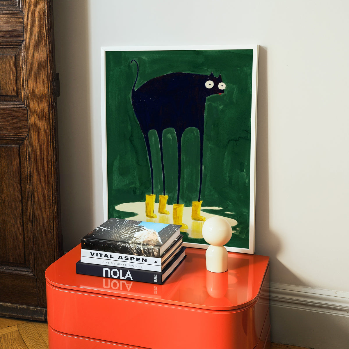 Funny cat in boots print in a white frame on a glossy orange cabinet with books