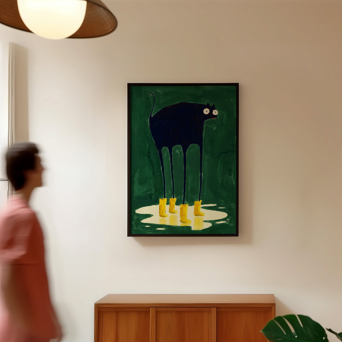 Googly-eyed black cat print in a black frame in a hallway under a rattan pendant