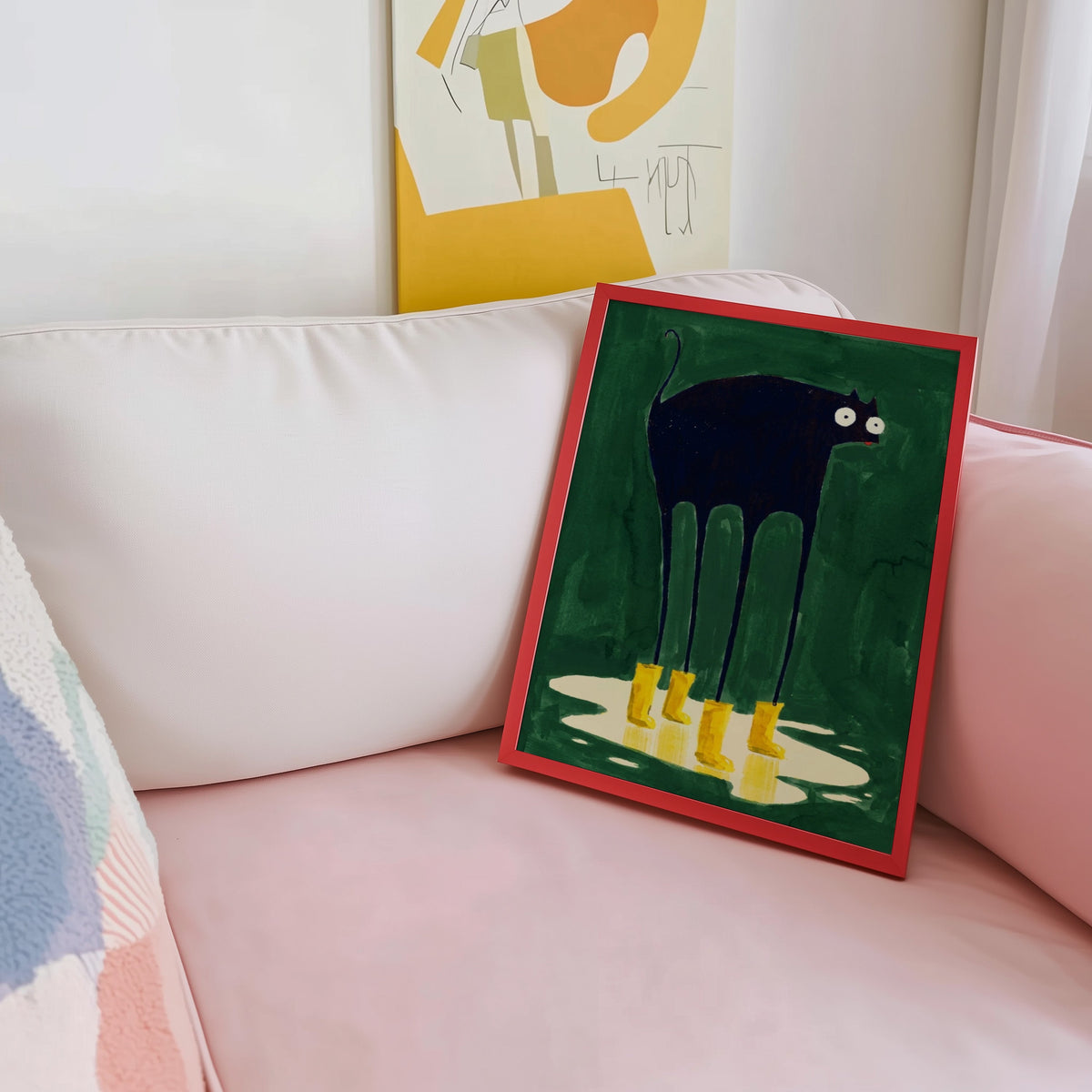 Yellow boots cat print shown in a red frame leaning on a blush pink sofa