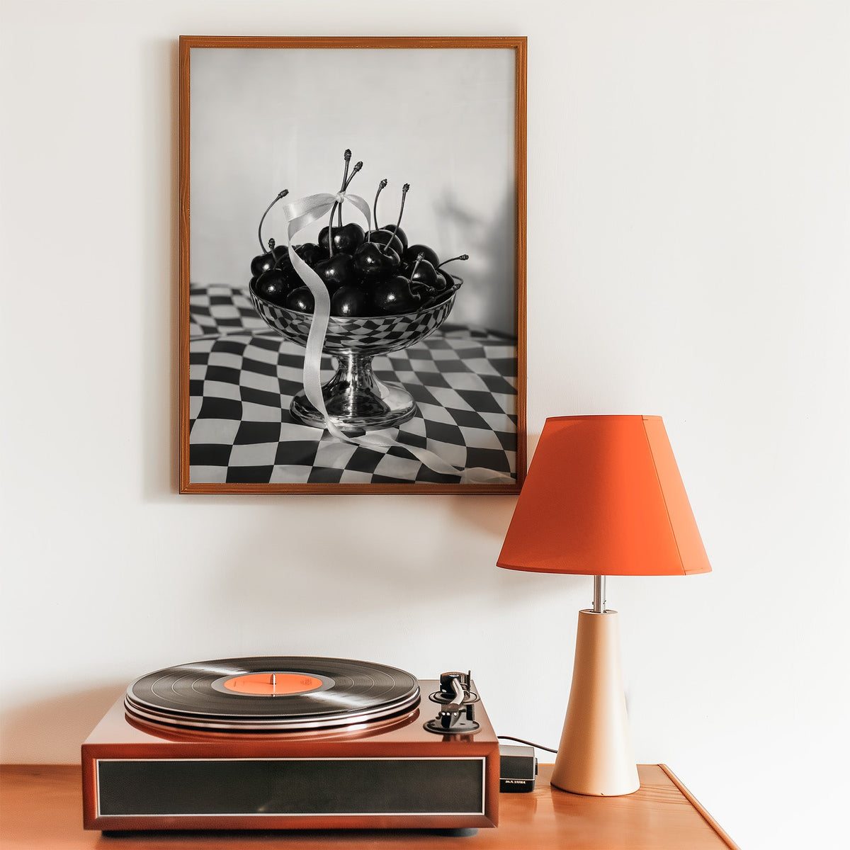 Black cherries in footed silver bowl print in a walnut frame above a record player and orange lamp