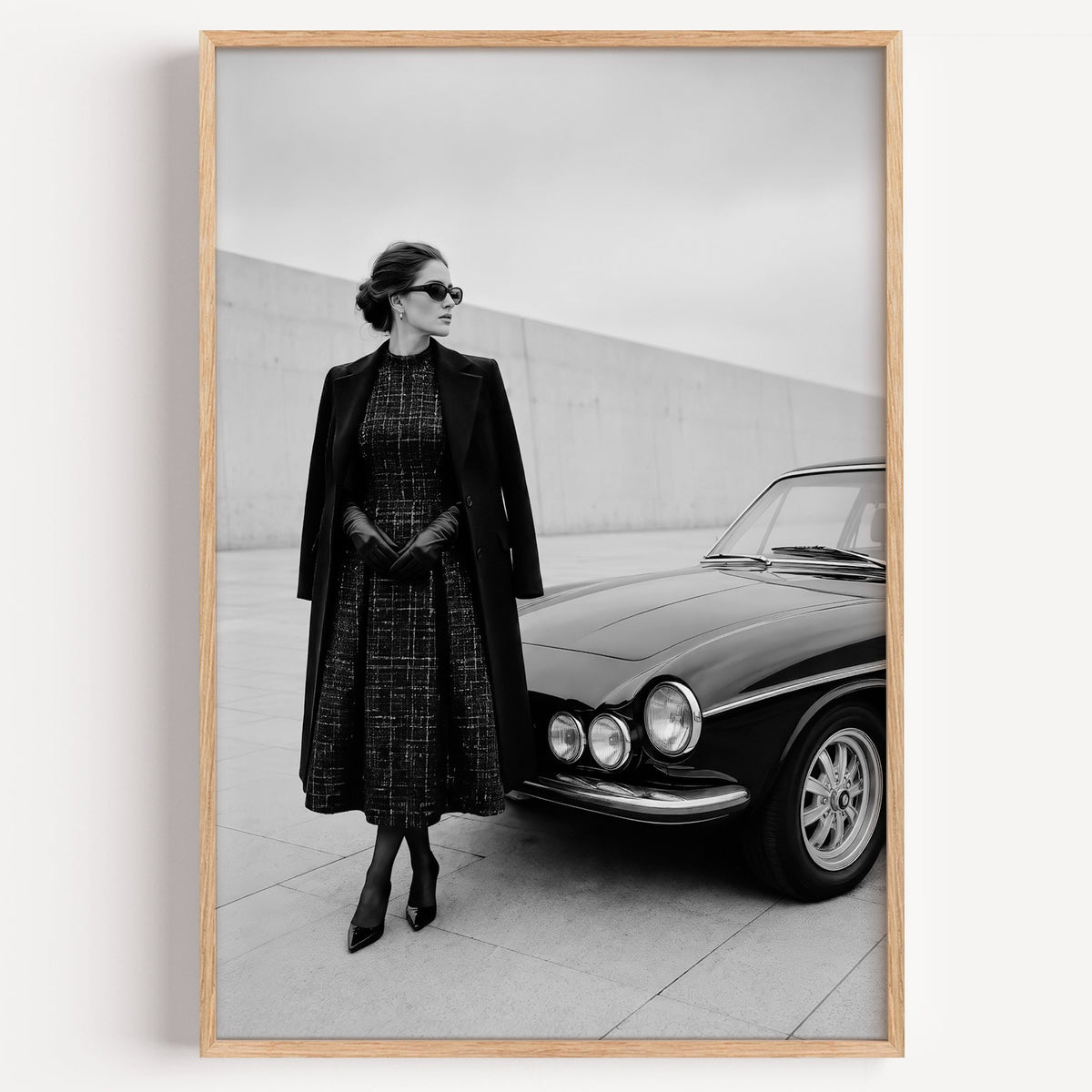 Black and white woman in tweed coat by classic car print in a light oak frame on a plain white wall