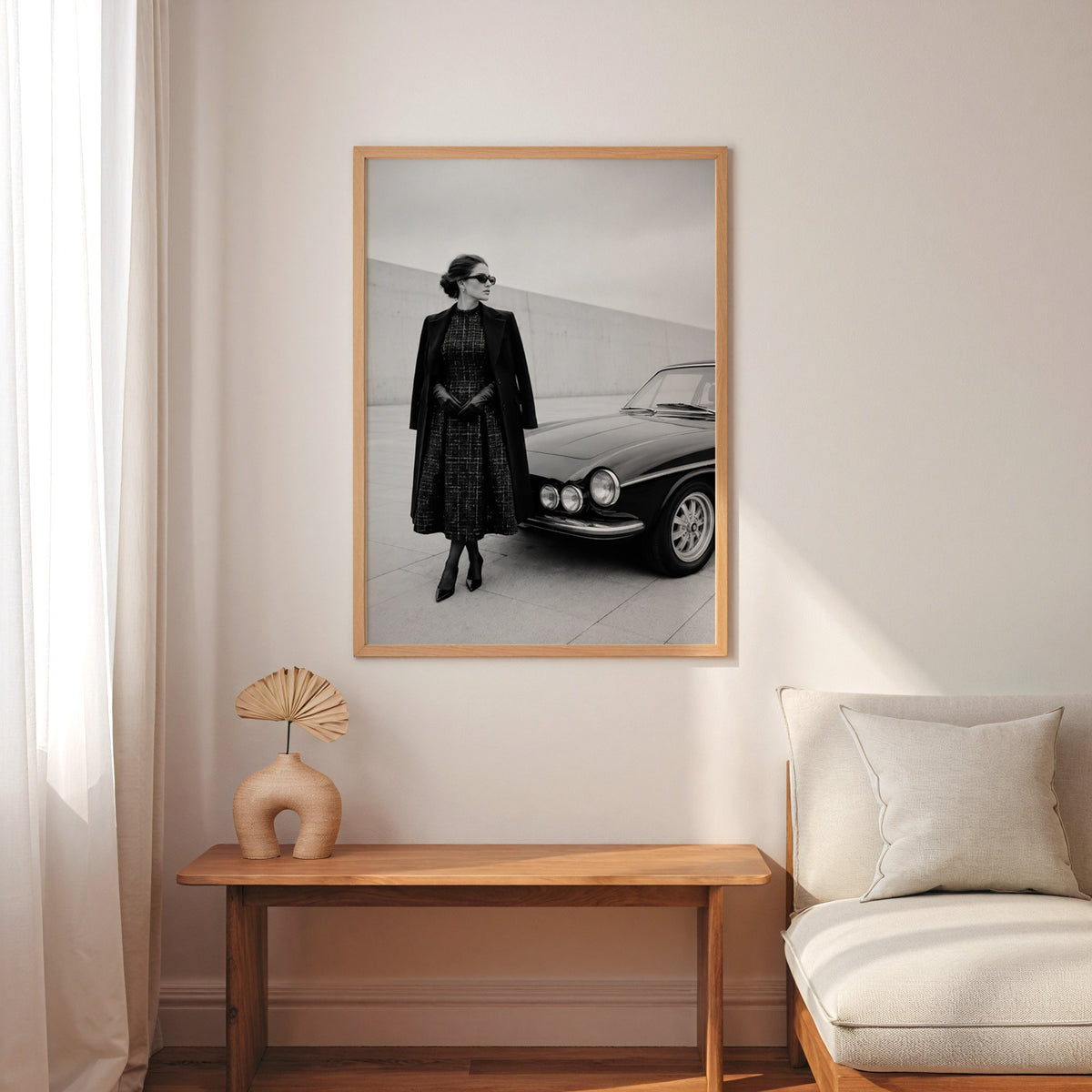 Black and white woman in tweed coat by classic car print in an oak frame above a narrow console with an arched vase
